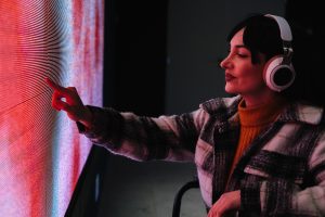 Woman in wheelchair reaching out to touch a colorful digital screen at an interactive art exhibit.